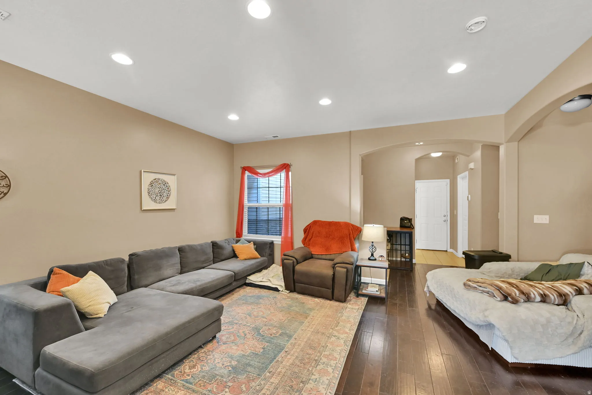 Recessed lighting illuminates the open living area featuring wood-finish flooring and a window with blinds