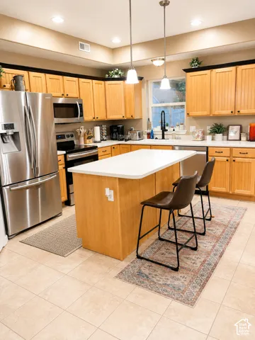 Recessed lighting illuminating the kitchen with wood-finish cabinetry, stainless steel appliances, and a central island with a white countertop