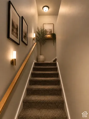 Carpeted staircase with a wood handrail, featuring wall-mounted sconces and a ceiling light fixture