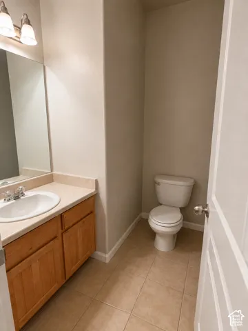 Neutral wall paint with white trim, a single-sink vanity with wood-finish cabinetry, a light-toned countertop, and tiled flooring
