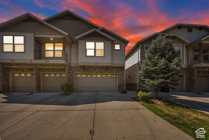 Townhome exterior featuring stone and siding finishes, individual garage access, and a second-story balcony with metal railings