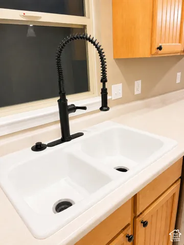 Dual-basin white sink with a matte black pull-down faucet, set into a light-toned countertop, complemented by light wood-finish cabinetry