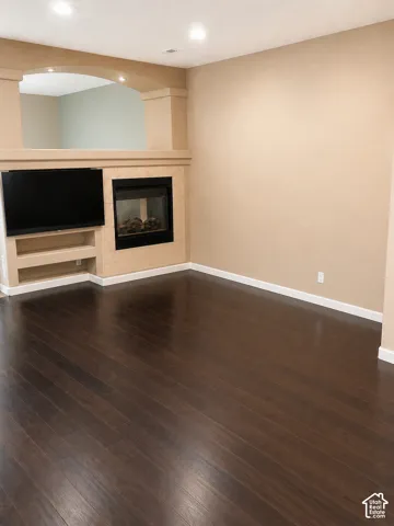 Dark wood-finish flooring, built-in media center with shelving, integrated fireplace, recessed lighting, and an arched architectural opening