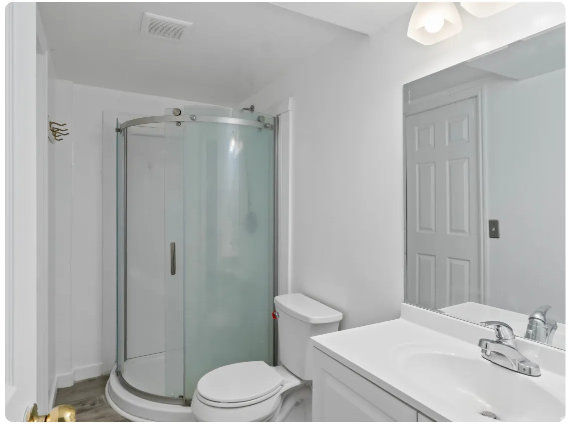 Bathroom featuring a corner shower with a curved glass enclosure, a white toilet, a vanity with an integrated sink, a chrome faucet, and a wall-mounted mirror