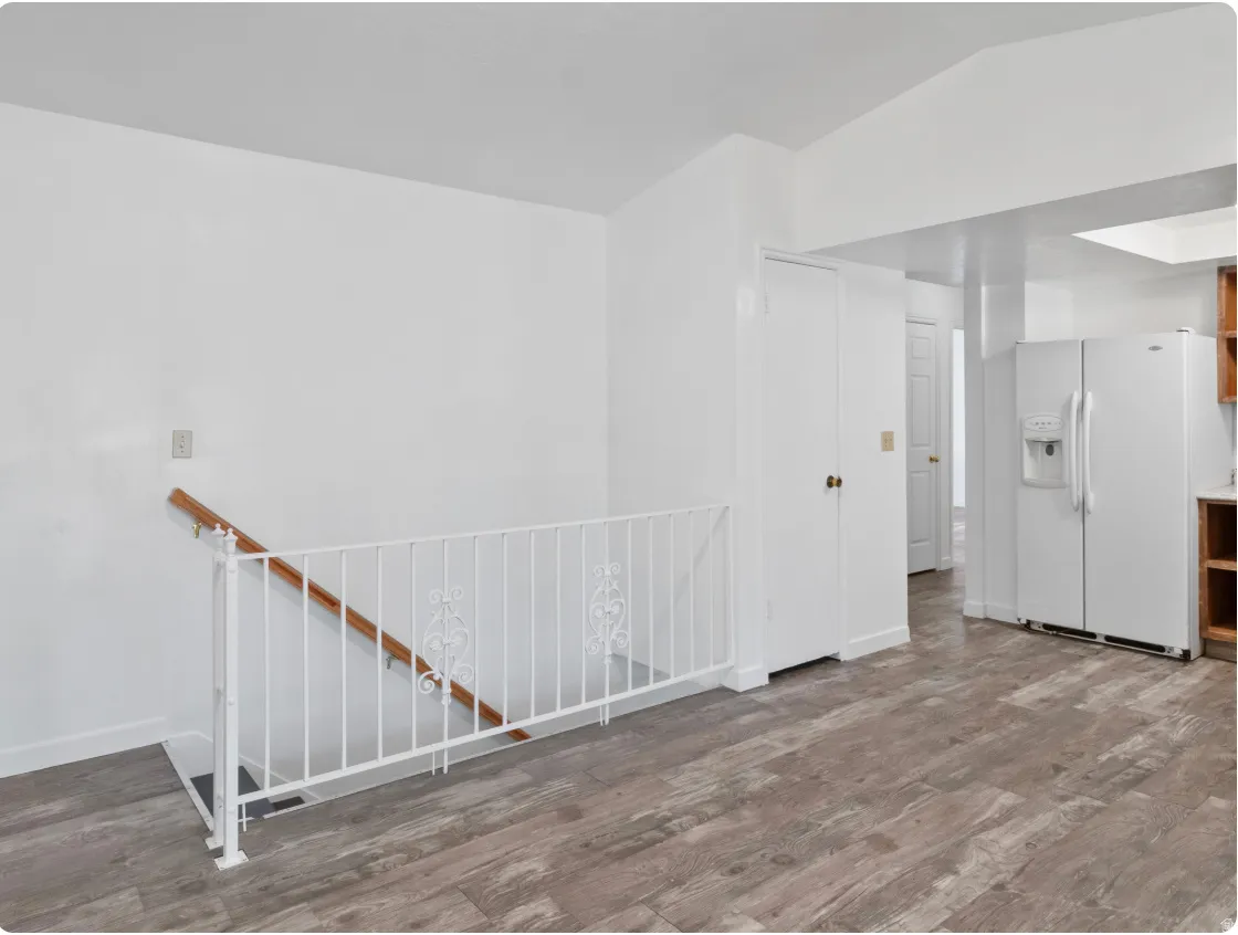 White interior walls, wood-finish flooring, white metal stair railing with wood handrail, built-in white closet, and a white refrigerator