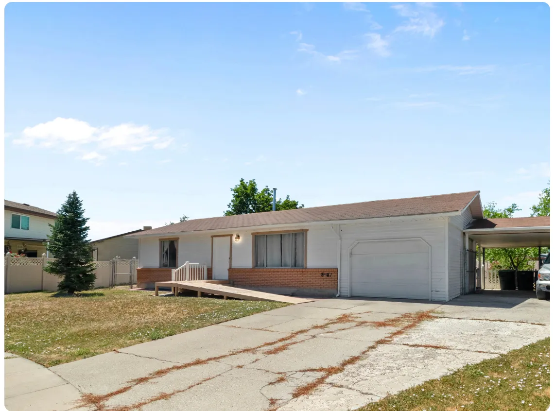 Single-story residence featuring a white siding exterior with brick accents, an attached garage, a covered carport, and a front entry ramp