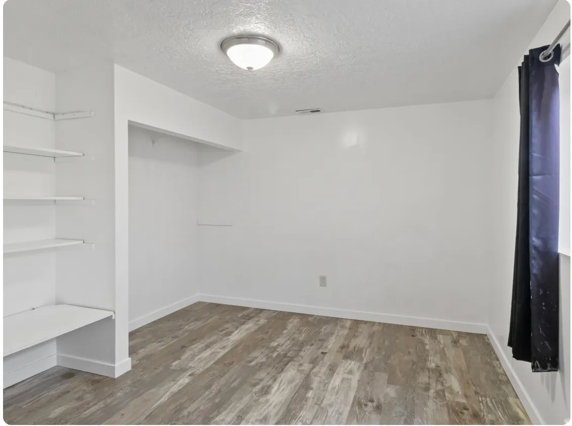 White walls with wood-finish flooring, featuring built-in shelving, a recessed clothing rod, and a ceiling-mounted light fixture