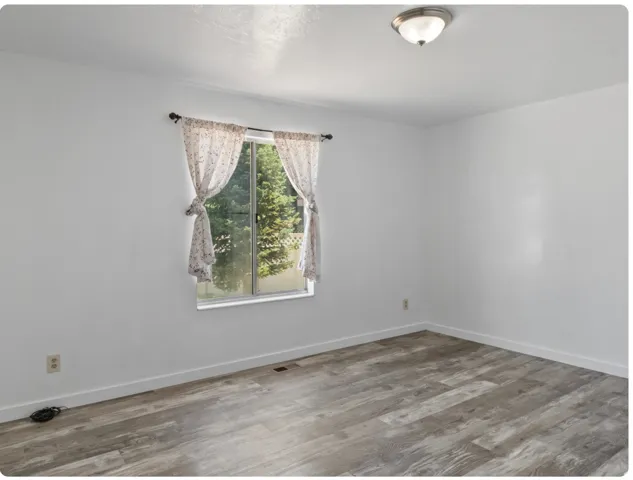 Window with outdoor scenery, overhead flush mount light fixture, wood-finish flooring, and white walls