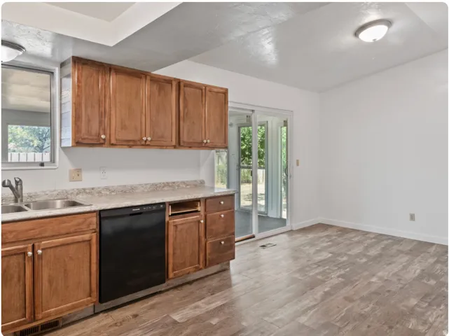 Wood-finish flooring throughout, featuring wood cabinetry, a double basin sink, and a black dishwasher
