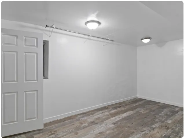 Recessed window, white paneled door, wood-finish flooring, two flush-mount ceiling lights, and integrated storage rod