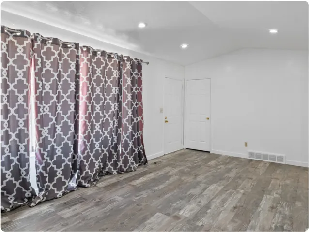 Vaulted ceiling with recessed lighting, wood-finish flooring, and white interior doors