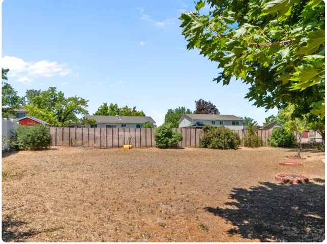 Expansive backyard featuring a wood fence, mature trees, and a clear sky