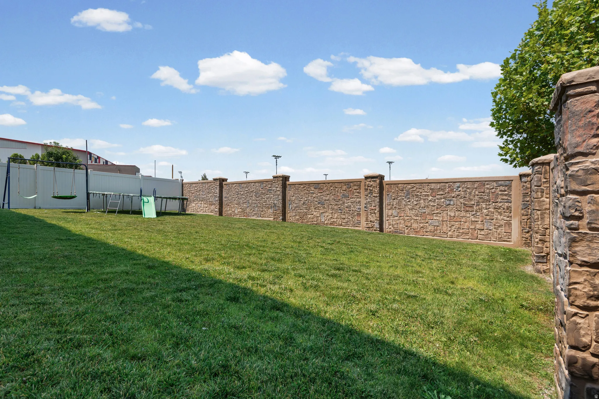 Expansive green lawn with a textured stone privacy wall and integrated lighting posts