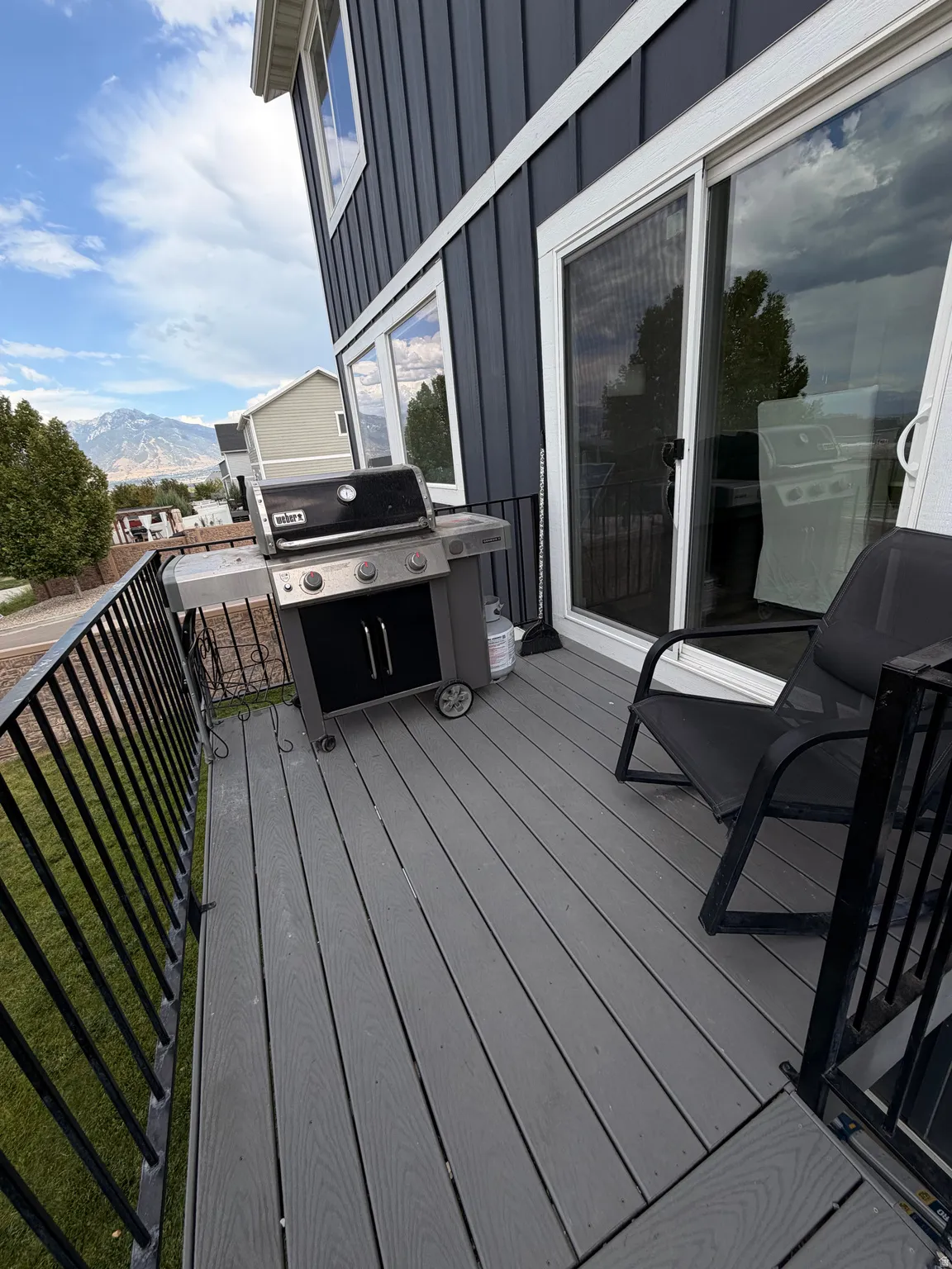 Composite deck with black metal railing, sliding glass door access, and dark vertical siding