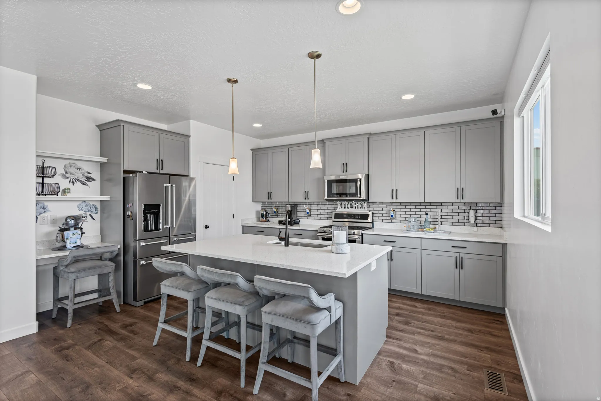 Kitchen with wood-finish flooring, gray cabinetry, stainless steel appliances, a center island with pendant lighting, and a subway tile backsplash