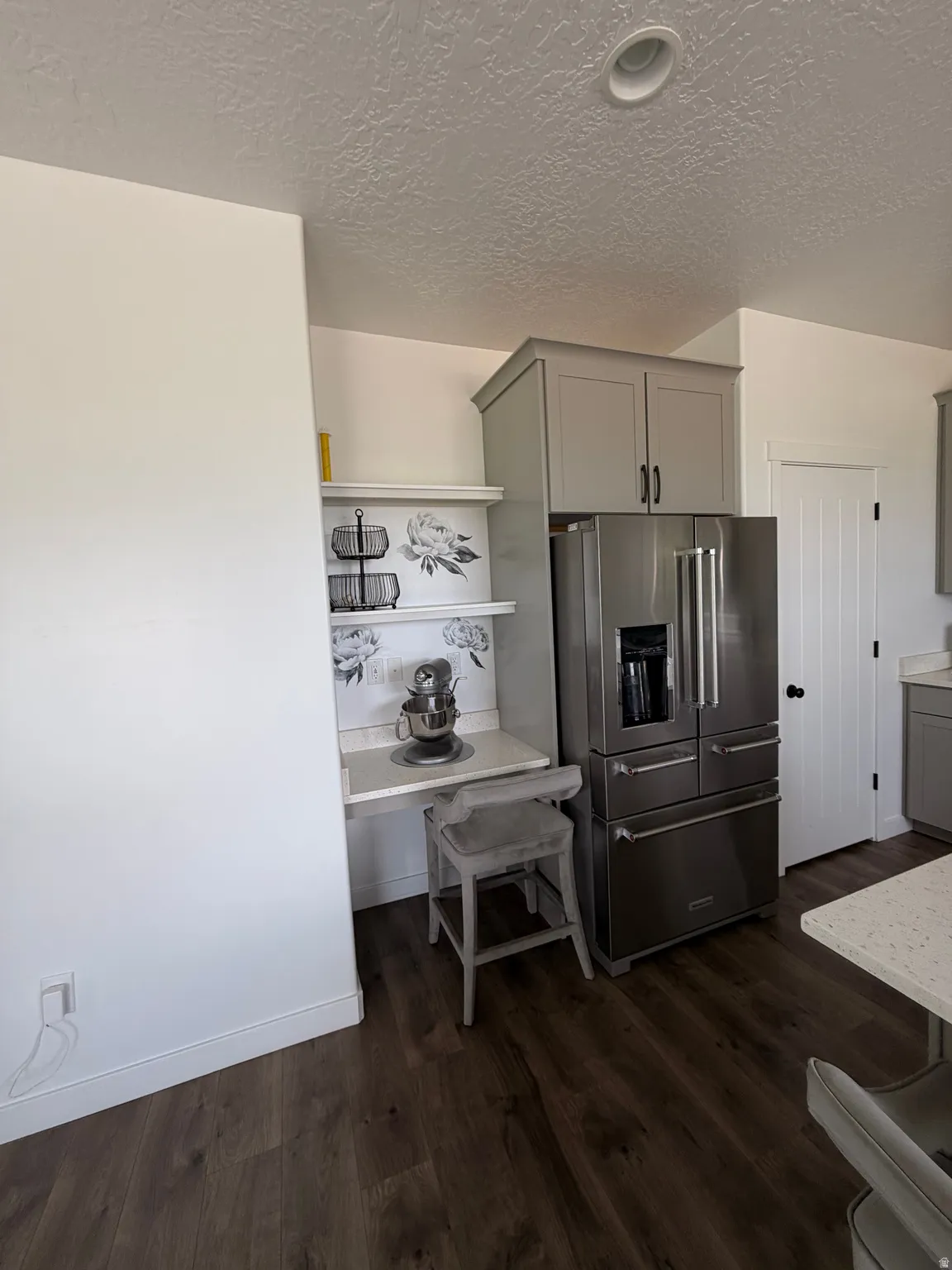 Modern kitchen featuring stainless steel French-door refrigerator with ice and water dispenser, wood-finish flooring throughout, built-in cabinetry with dark hardware, and open layout with dedicated workspace and shelving