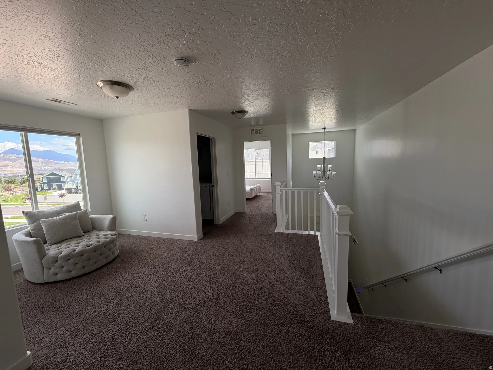 Expansive carpeted landing featuring a prominent window, white painted walls, and a staircase with a white balustrade