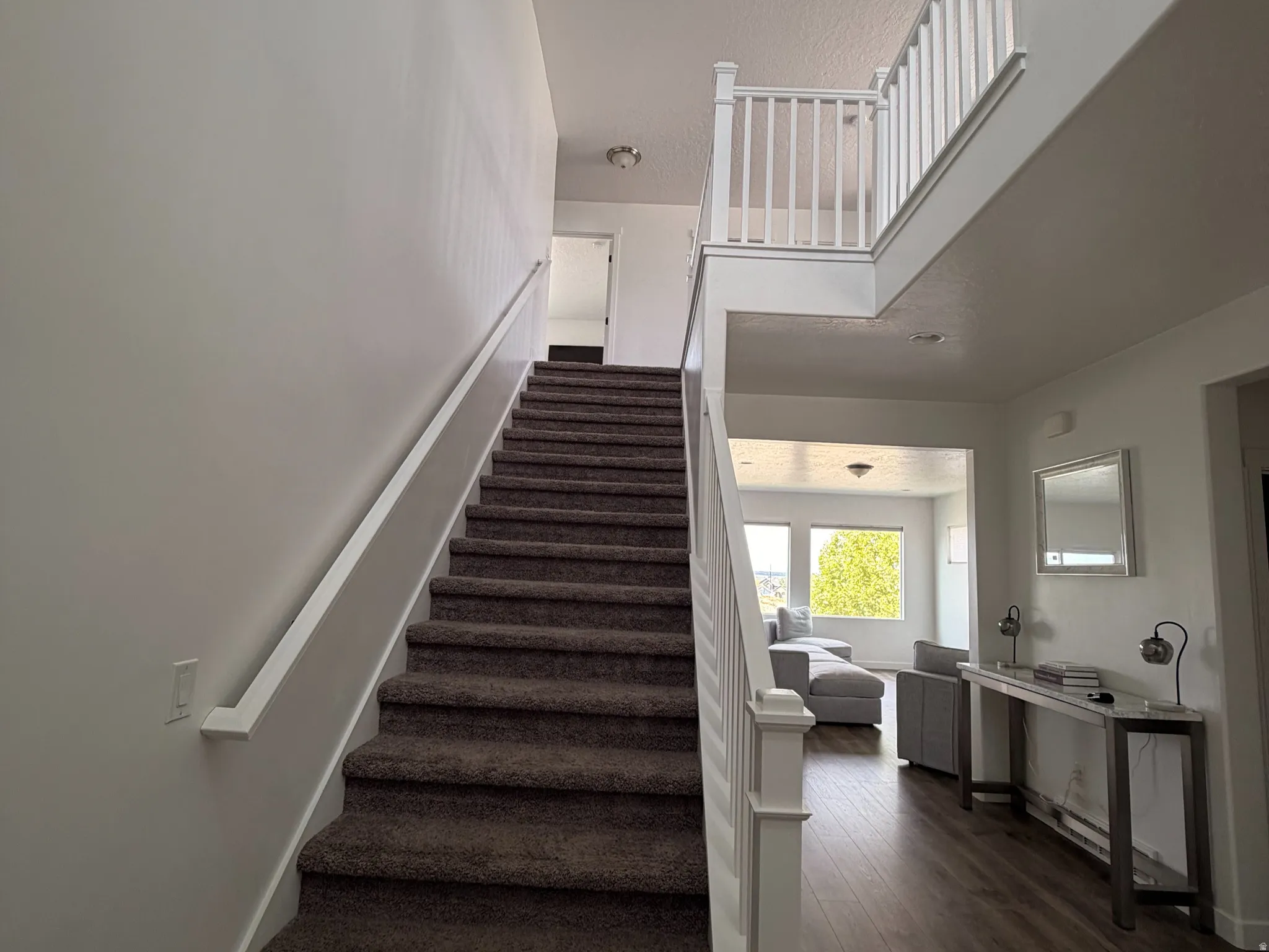 Carpeted staircase with white railings, wood-finish flooring, and a second-story landing with white balusters
