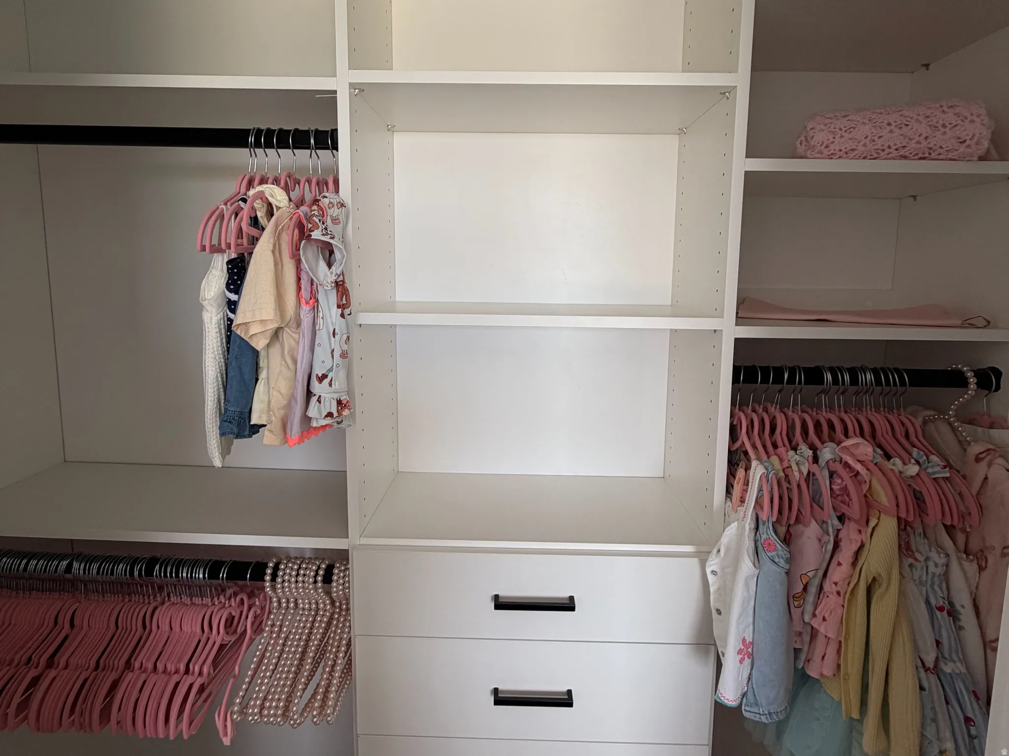 Built-in closet system featuring multiple shelves, hanging rods, and a five-drawer dresser with matte black pulls