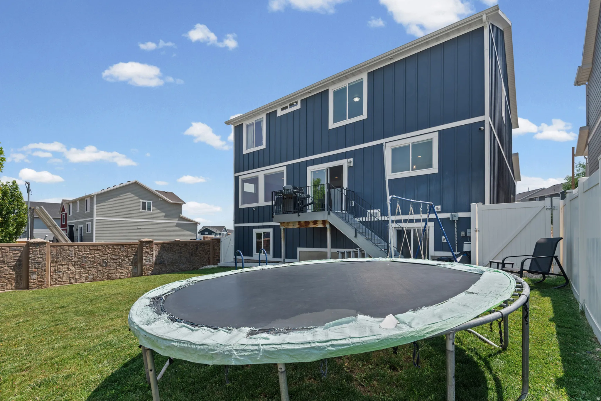 Spacious fenced backyard with green lawn, stone-finish wall, and private deck with stairs