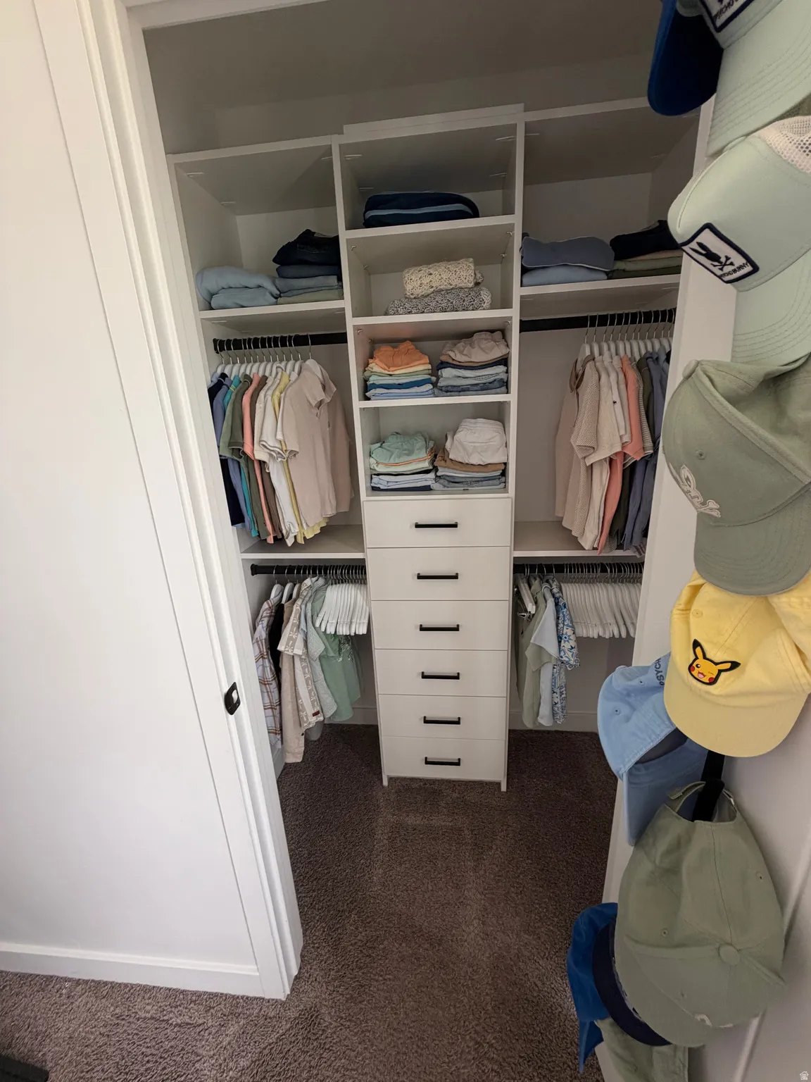 Custom closet system featuring built-in shelving, hanging rods, and a central drawer unit with dark hardware