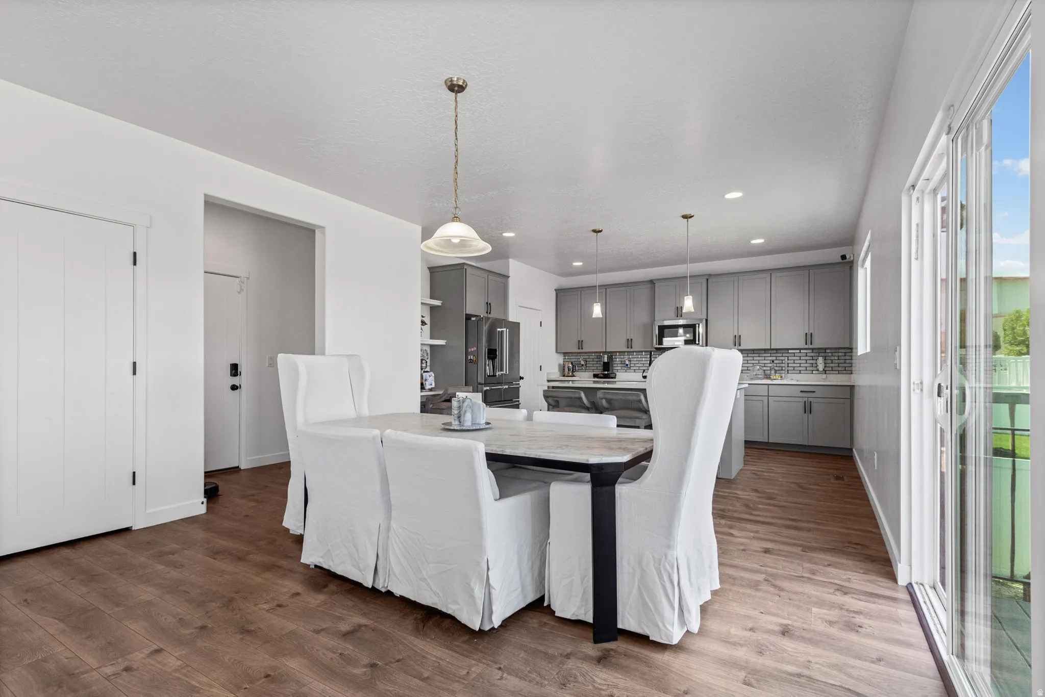 Wood-finish flooring throughout, bright white walls, contemporary gray cabinetry, stainless steel appliances, and a sliding glass door