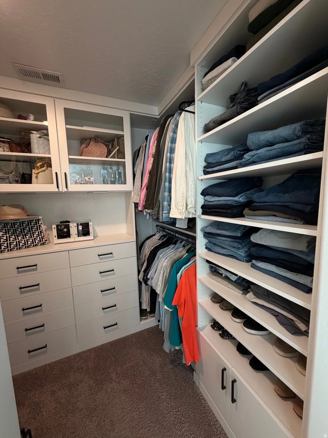 Custom closet system featuring built-in drawers, glass-front cabinetry, hanging rods, and open shelving