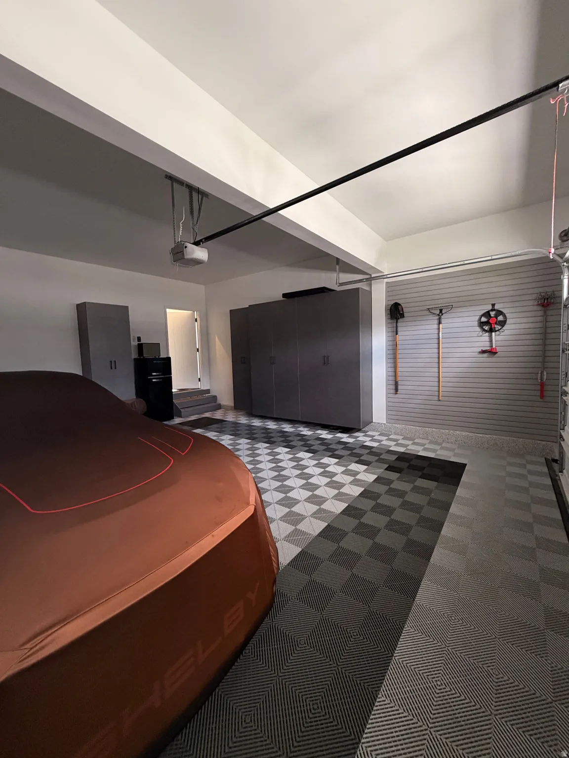 Garage featuring checkerboard flooring, built-in storage cabinetry, and slat wall organization system