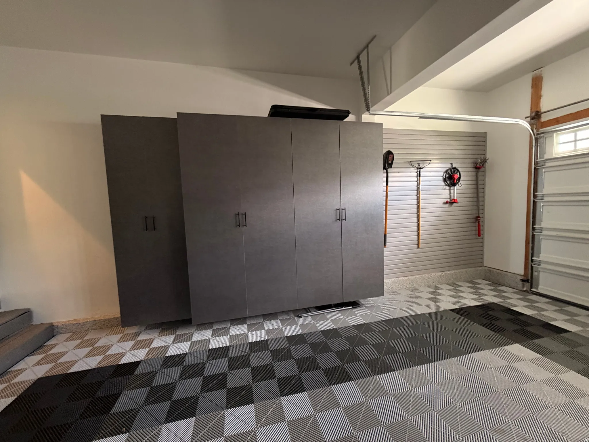 Checkerboard pattern floor tiling, wall-mounted storage system, built-in cabinetry, overhead garage door with upper window panes