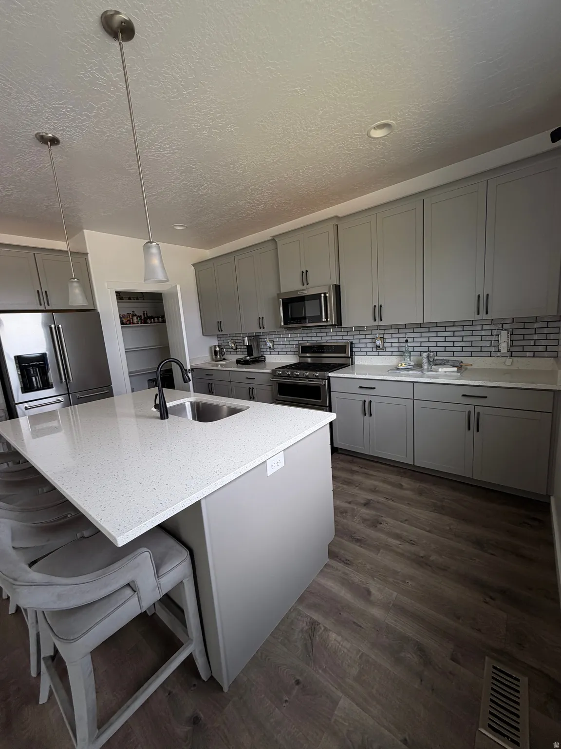 Kitchen featuring wood-finish flooring, light grey cabinetry, stone countertops, stainless steel appliances, and a subway tile backsplash