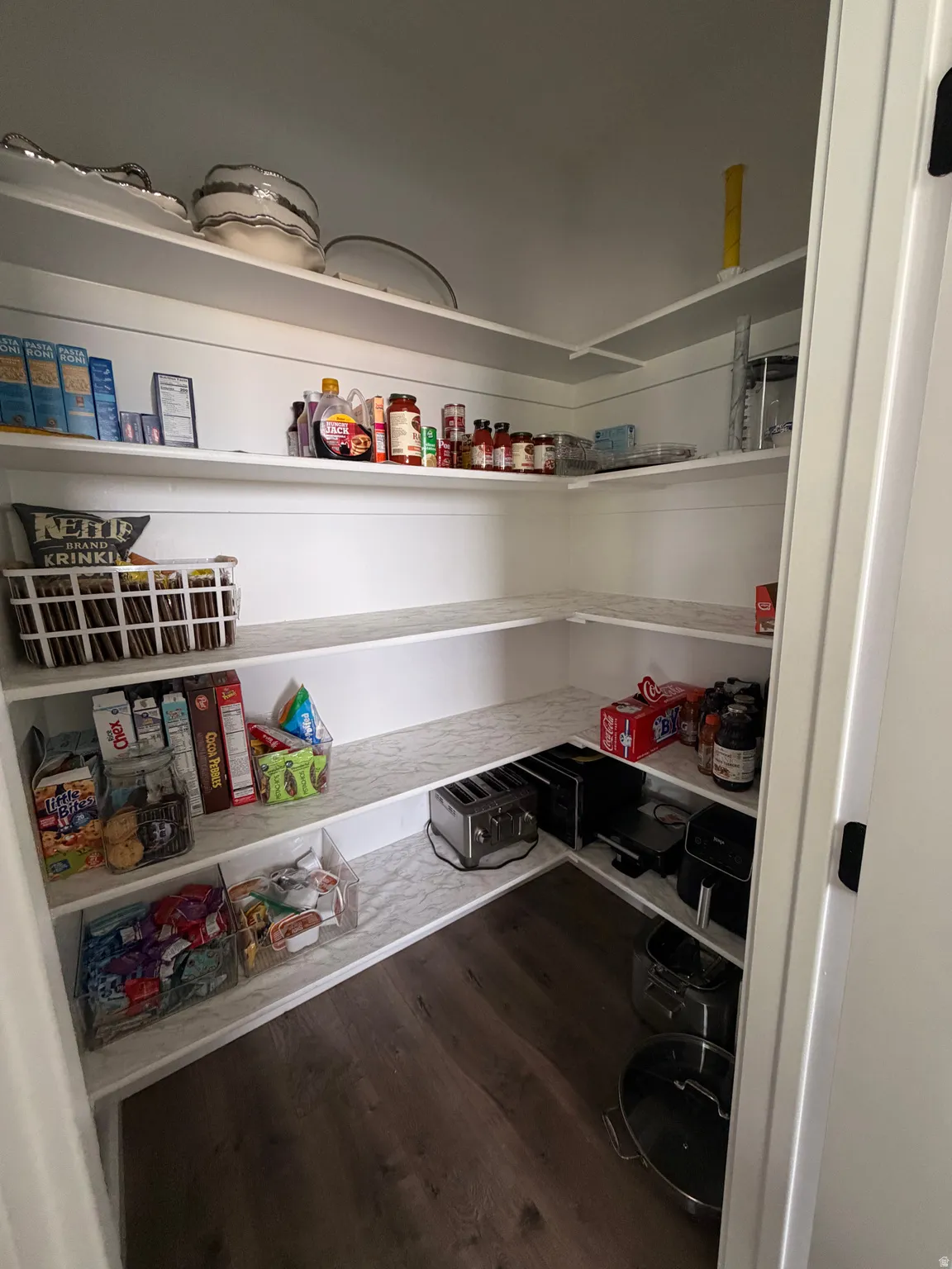 Walk-in pantry featuring built-in shelving, white finishes, and wood-finish flooring
