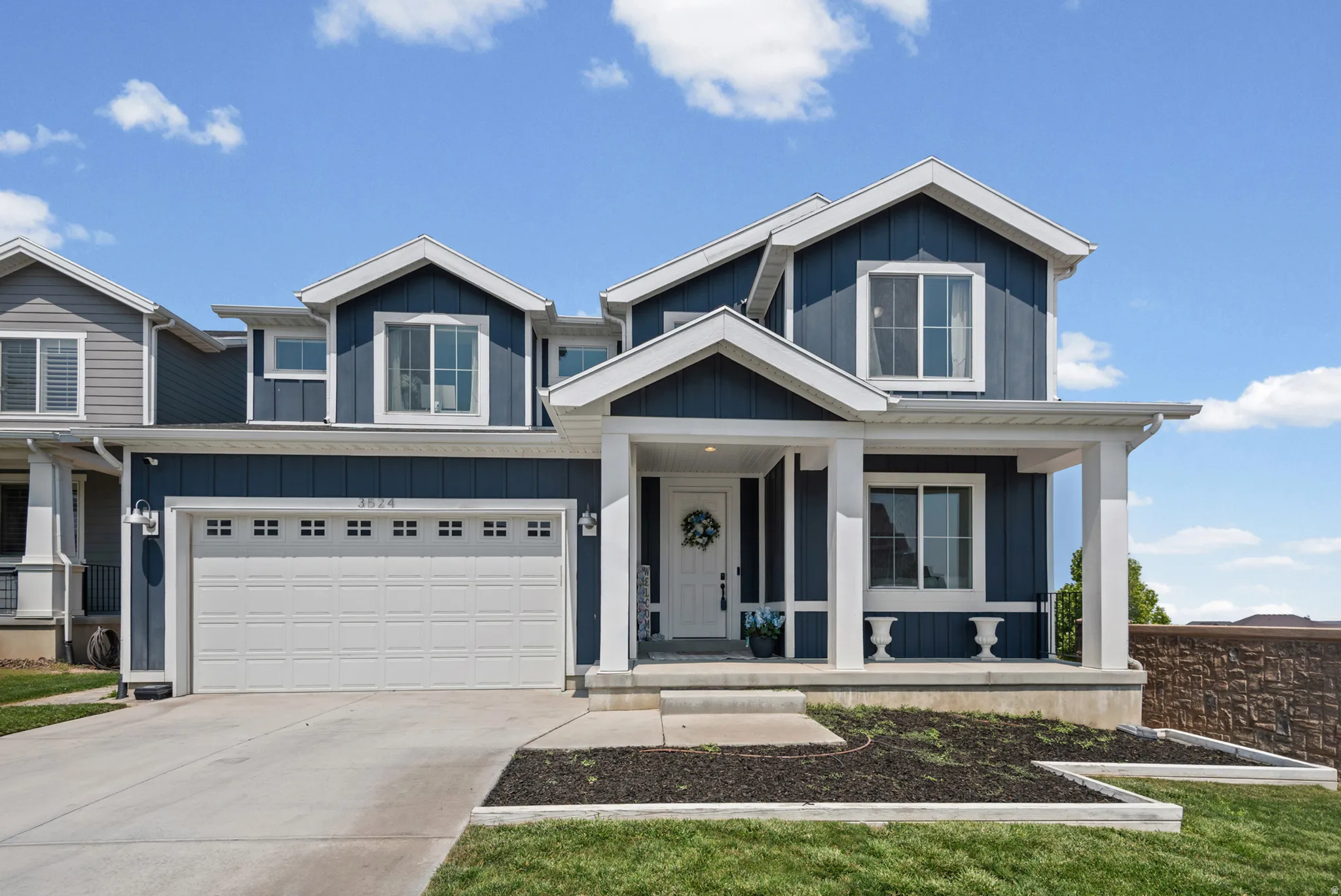 Two-story residence featuring a covered entry porch, white garage door, dark blue siding, white trim, and a concrete driveway