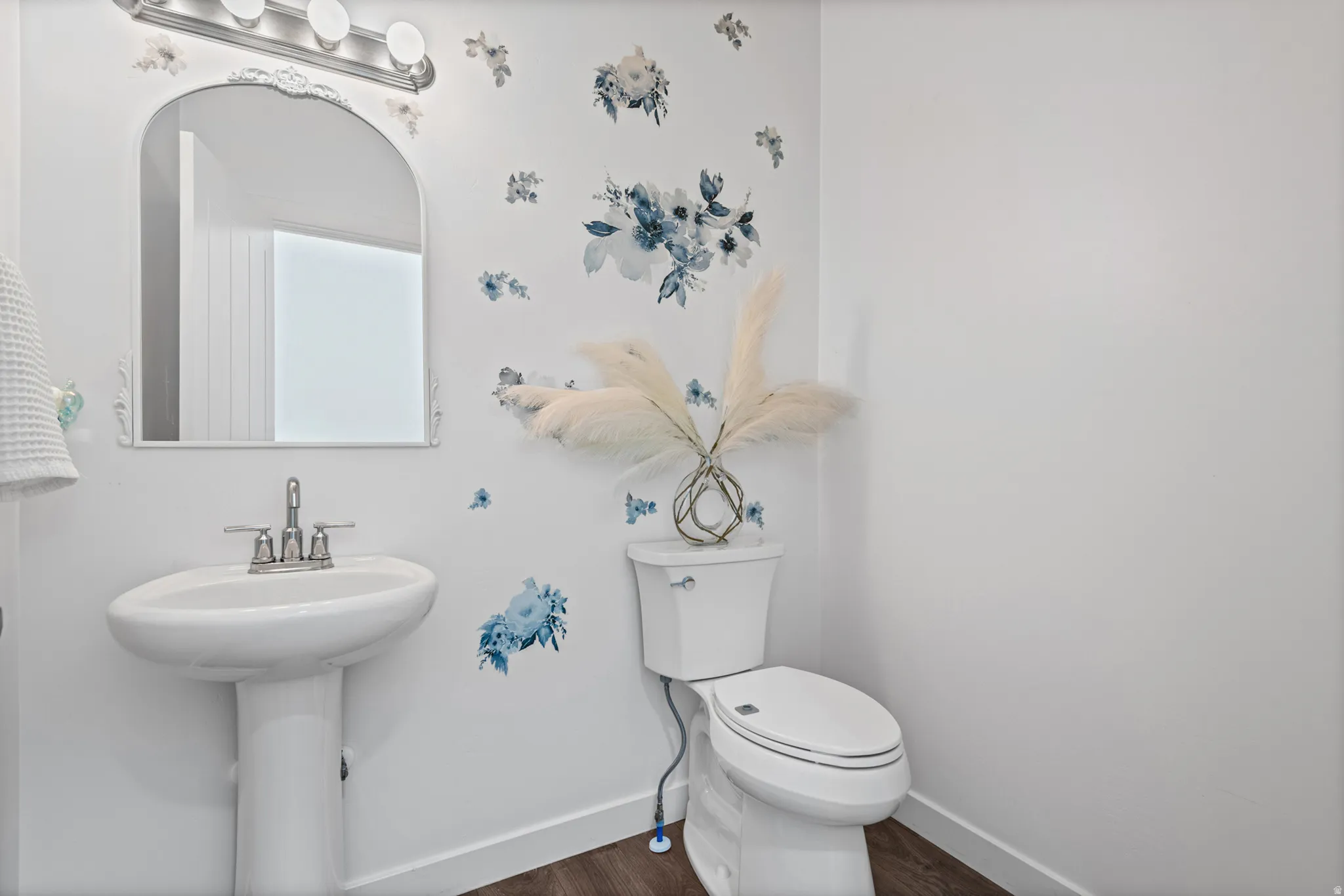 Pedestal sink with chrome-finish faucet, framed mirror, and wood-finish flooring
