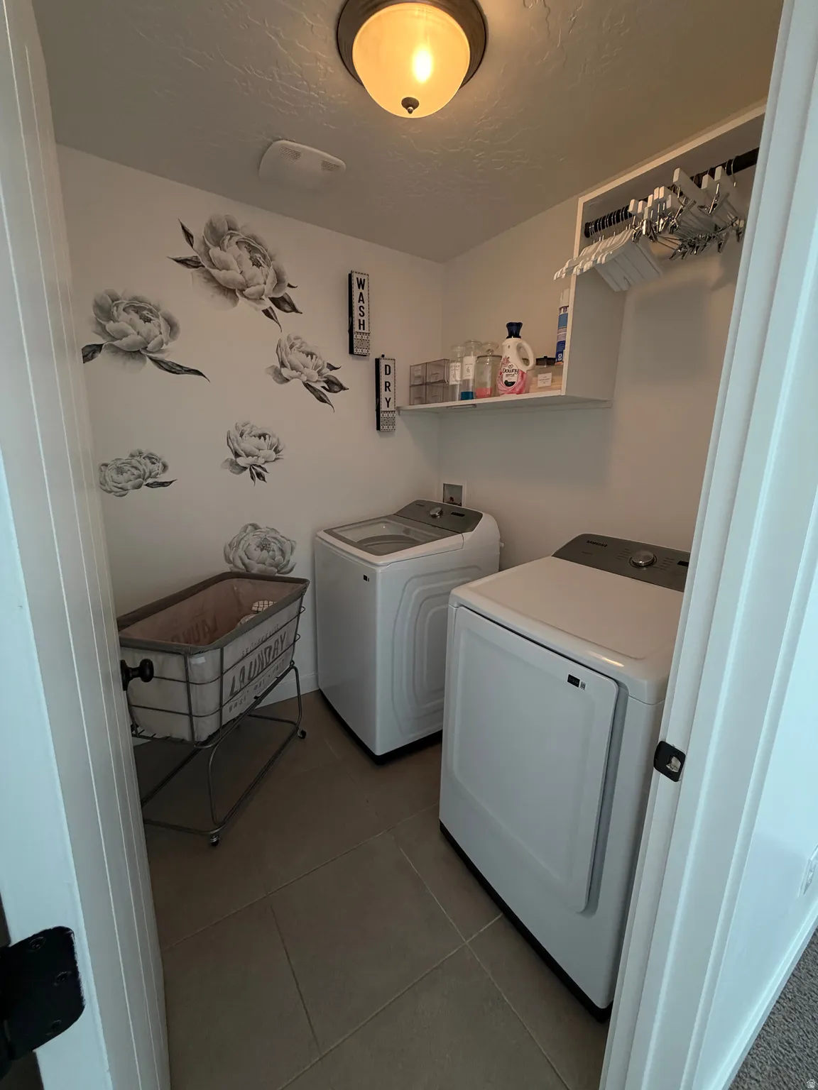 Integrated laundry area featuring neutral-toned floor tile and a built-in wall shelf