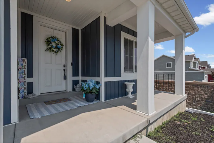 Covered front porch with white columns, concrete slab, and a stone-finish retaining wall