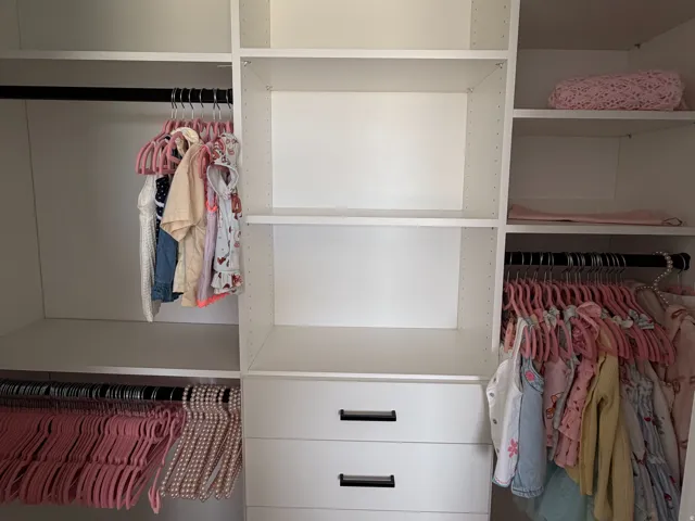 Built-in closet system featuring multiple shelves, hanging rods, and a five-drawer dresser with matte black pulls