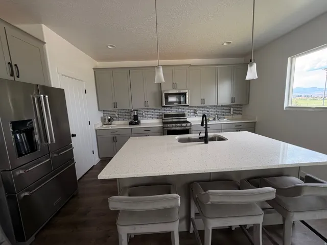 Stainless steel appliances, grey cabinetry, mosaic tile backsplash, central island with integrated sink, and wood-finish flooring