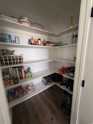 Walk-in pantry featuring built-in shelving, white finishes, and wood-finish flooring