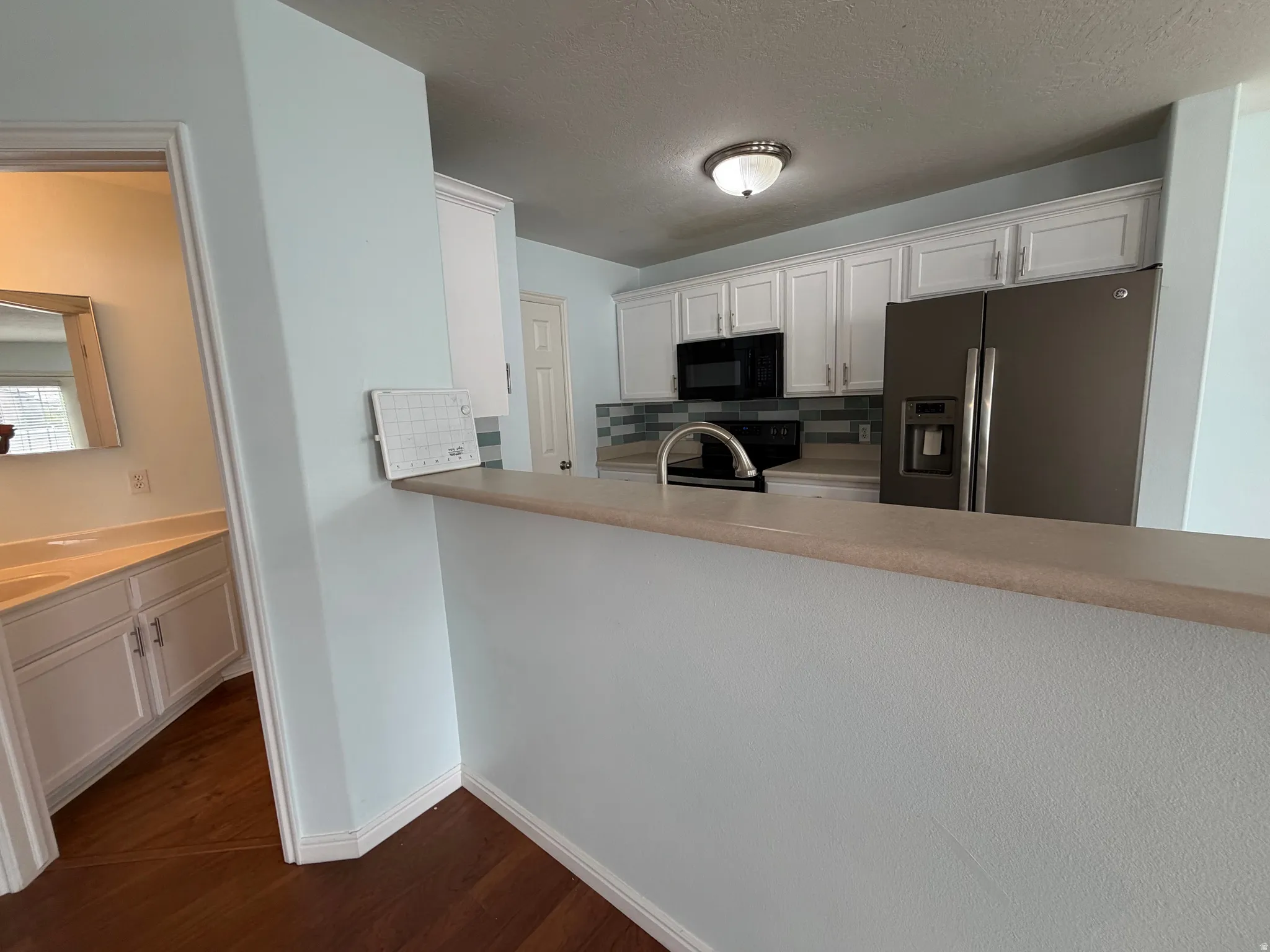 Kitchen featuring white cabinetry with silver-tone hardware, stainless steel refrigerator, black microwave, and a decorative tile backsplash