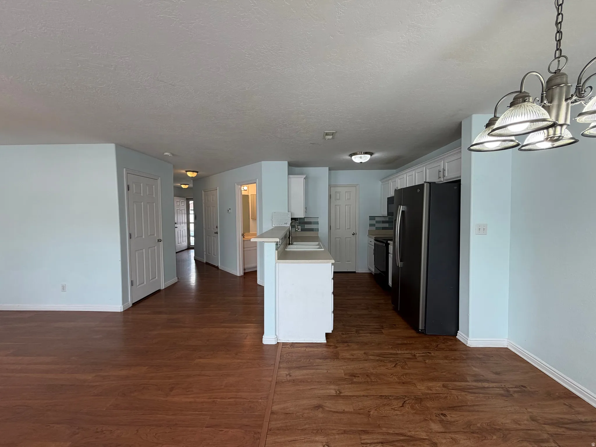 Wood-finish flooring throughout, white kitchen cabinetry, stainless steel appliances, light blue wall paint, and a multi-light chandelier