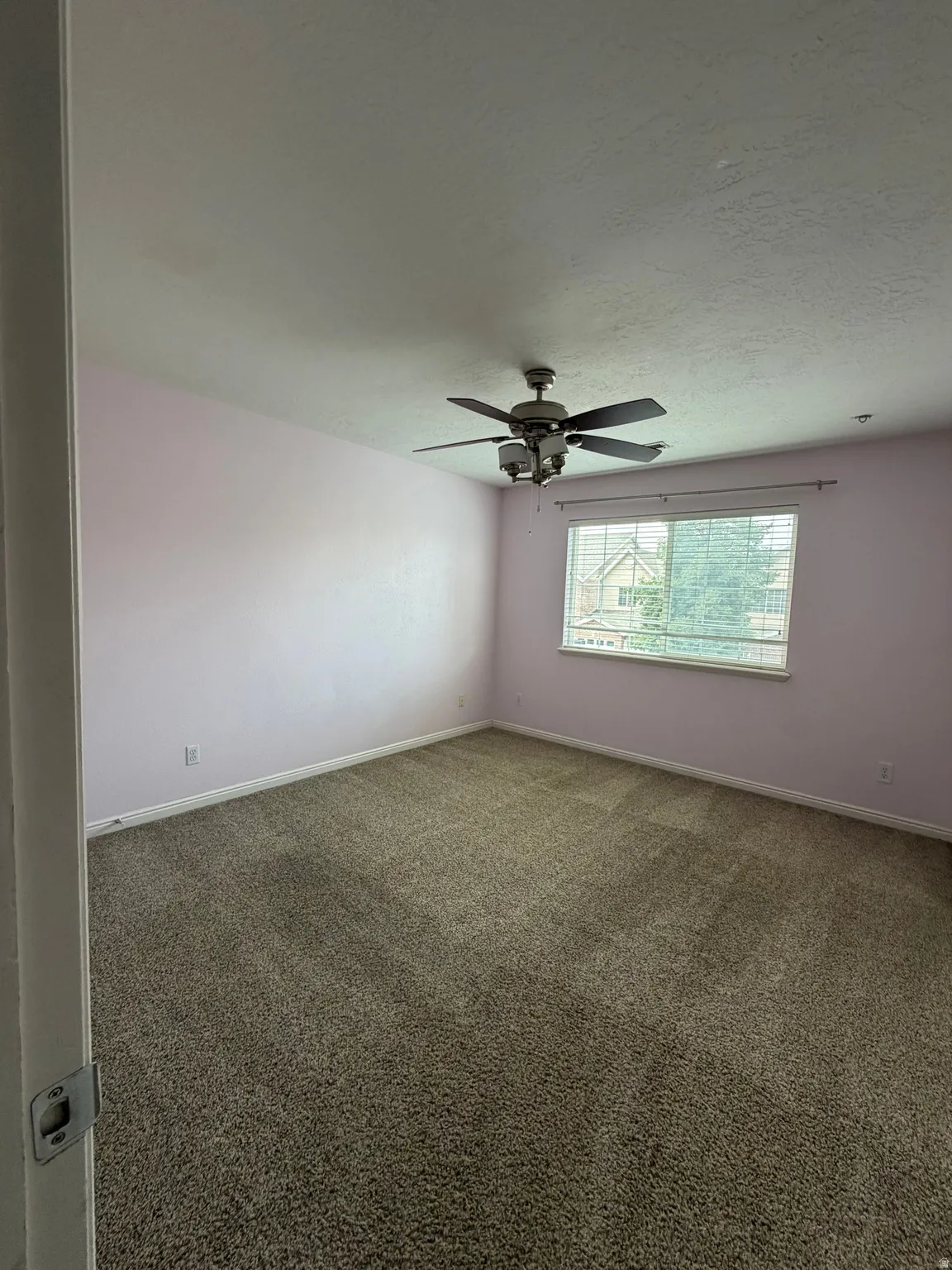 Textured carpeting, window with blinds, overhead ceiling fan with lighting, and light-colored wall paint