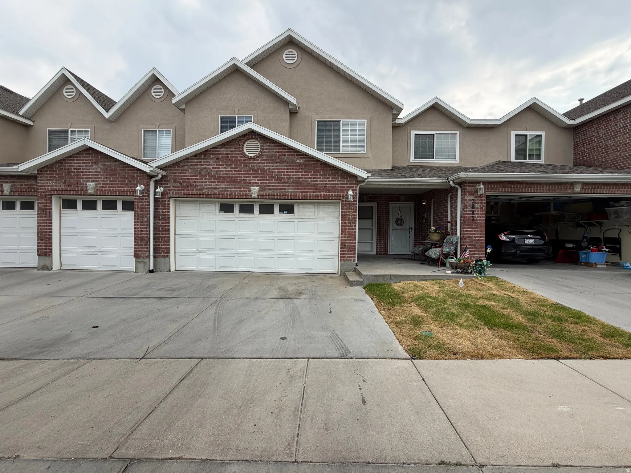 Two-story residence featuring brick and stucco exterior, multiple gables, white garage doors with window inserts, and concrete driveways