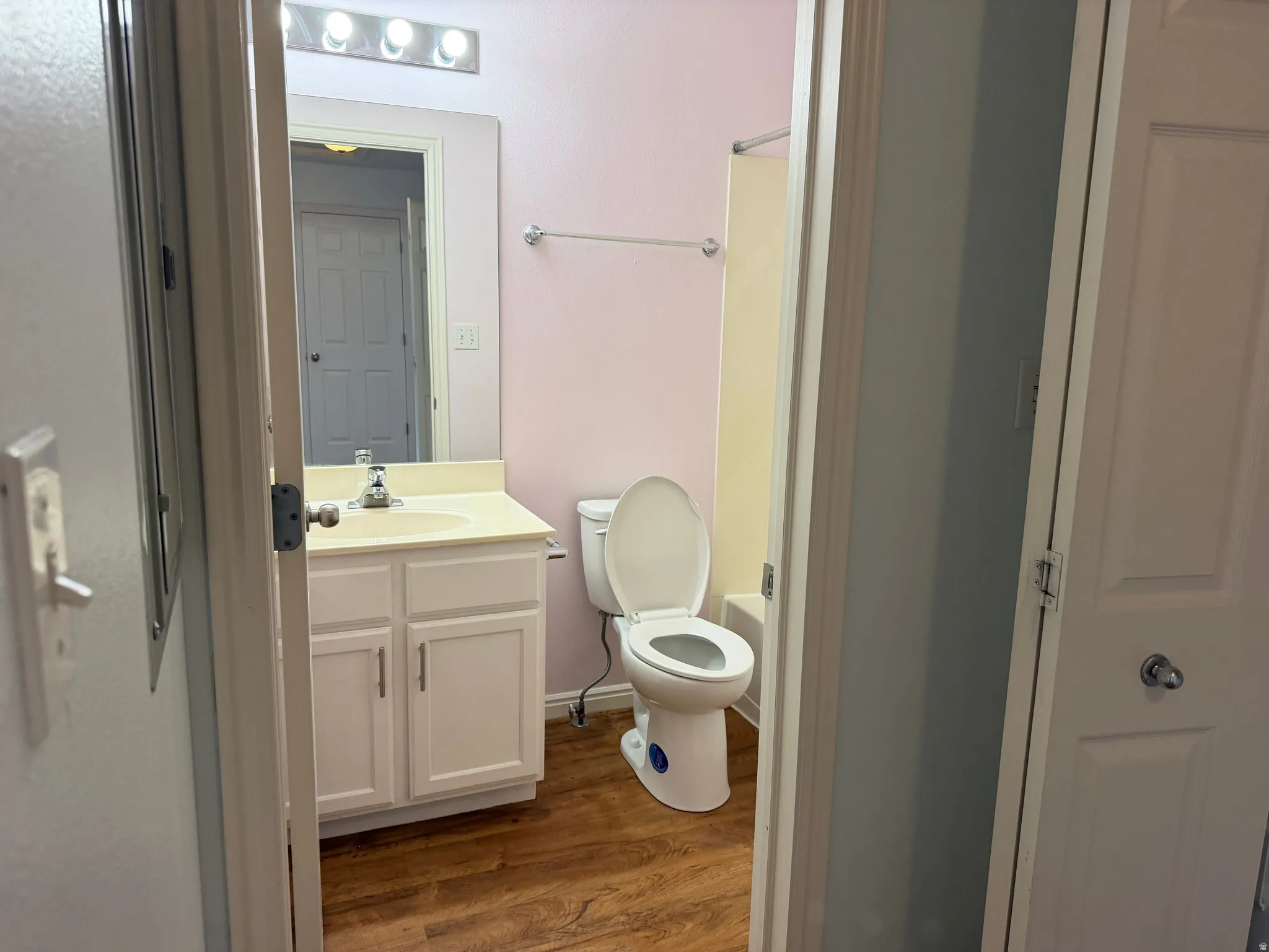 Bathroom featuring wood-finish flooring, a white vanity with integrated sink, and a wall-mounted light fixture