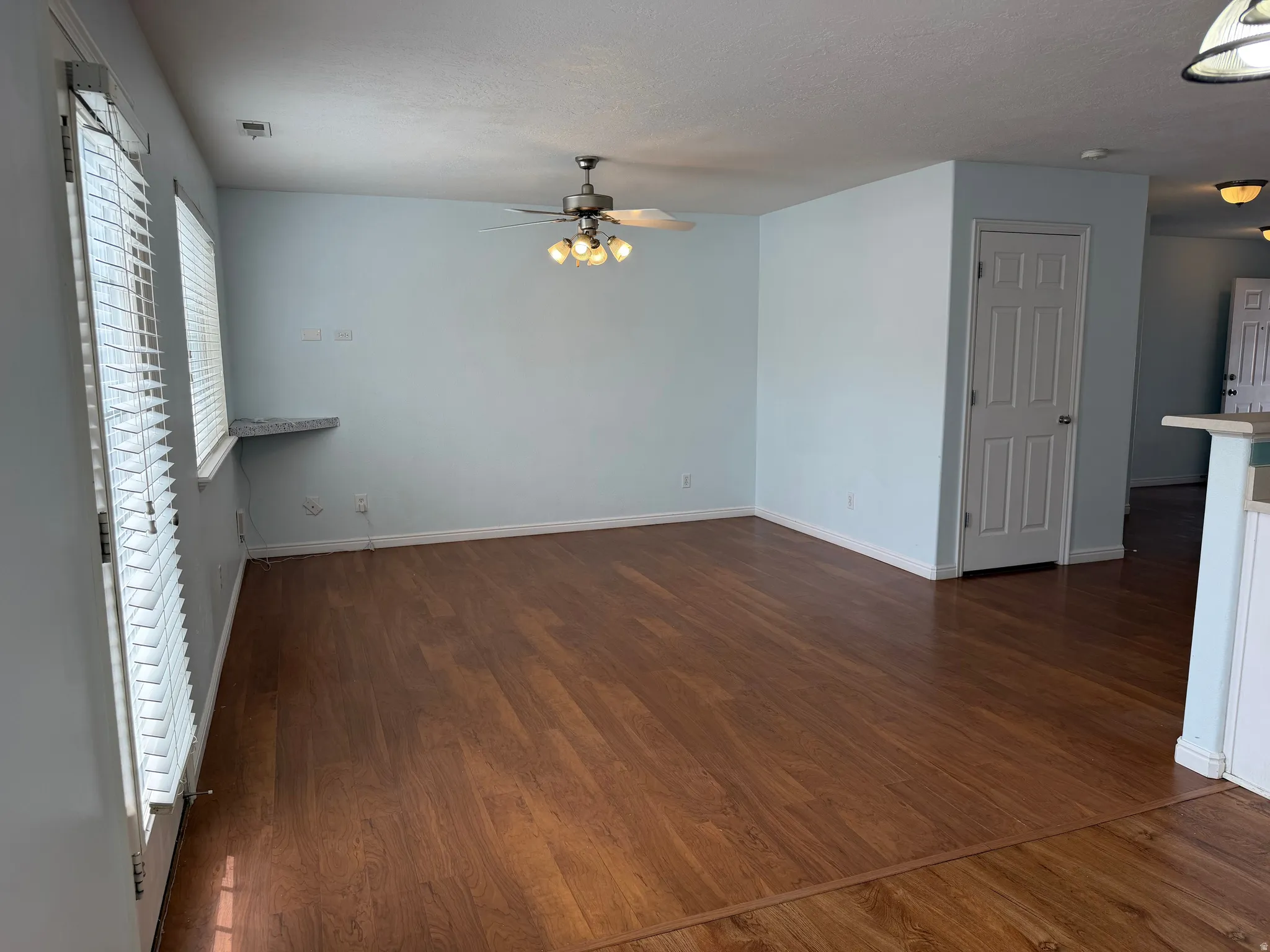 Spacious room featuring wood-finish flooring, a ceiling fan with integrated lighting, and multiple windows with blinds