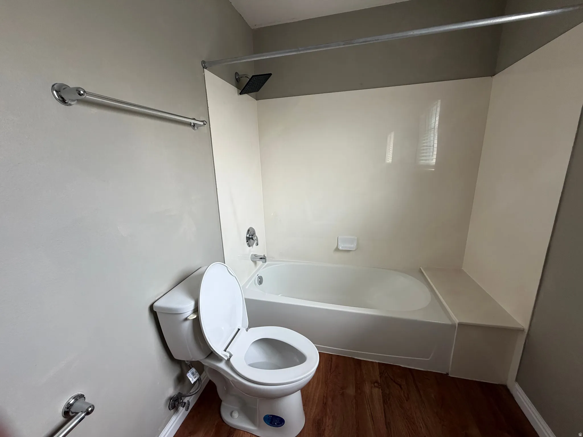 Tub and shower combination with a black shower head, white tiled surround, and wood-finish flooring
