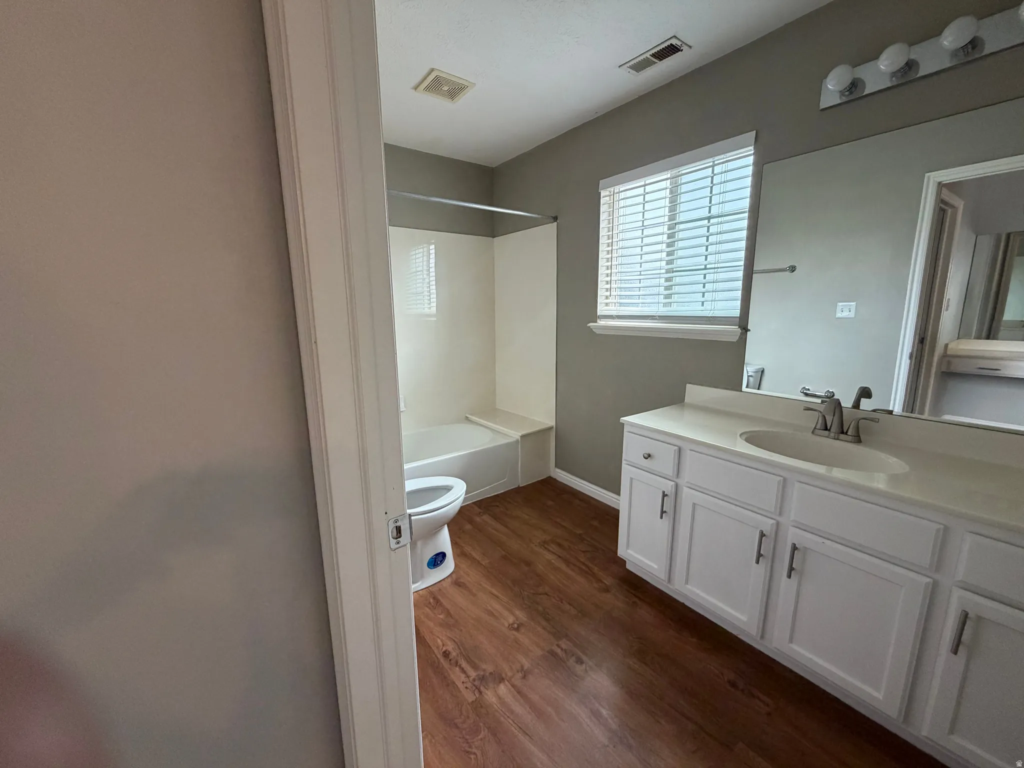 Bathroom featuring a single vanity with a white countertop, white cabinetry with silver-tone hardware, wood-finish flooring, and a shower/tub combination