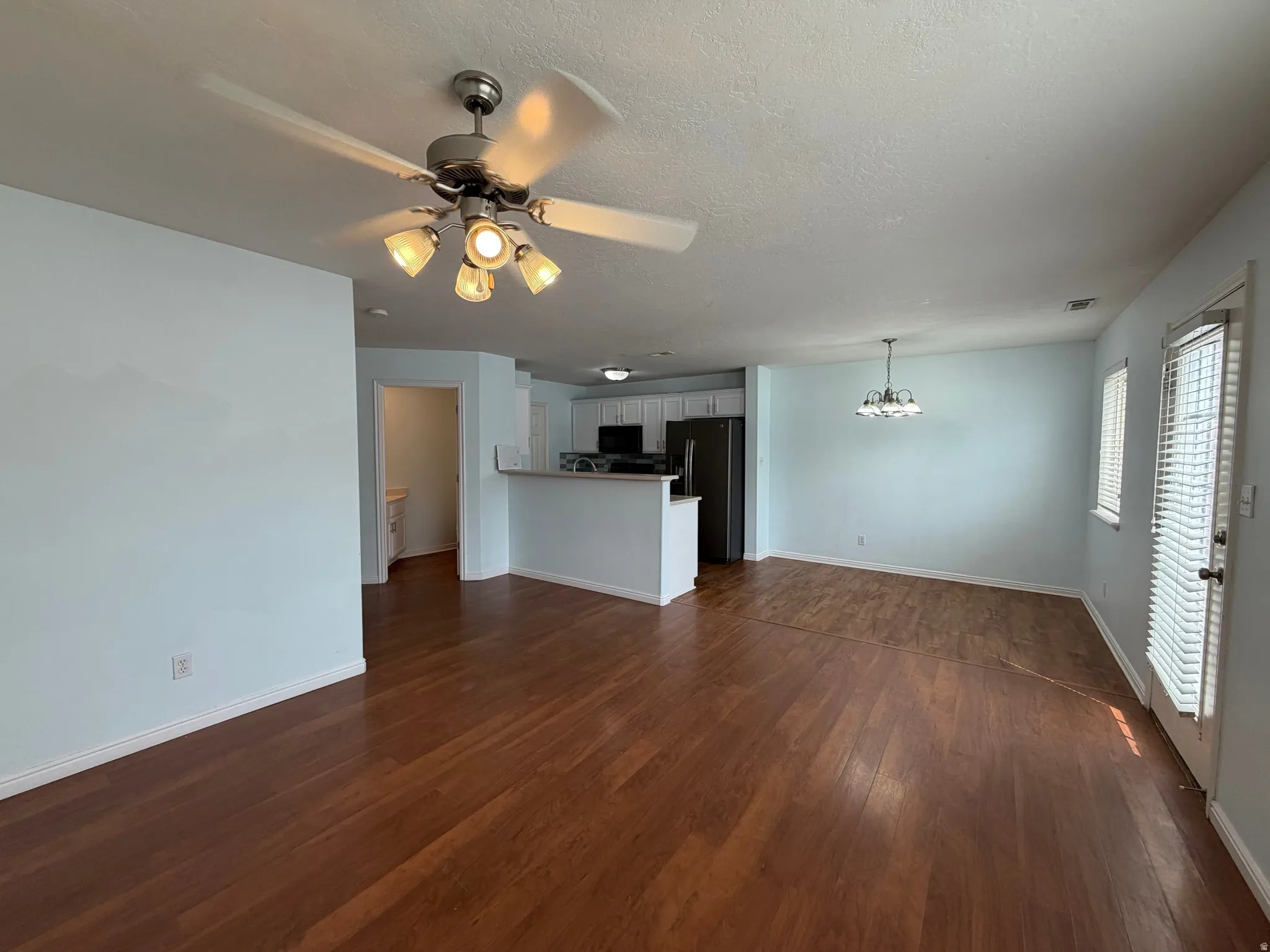 Open-concept living area with wood-finish flooring, a ceiling fan, and a breakfast bar