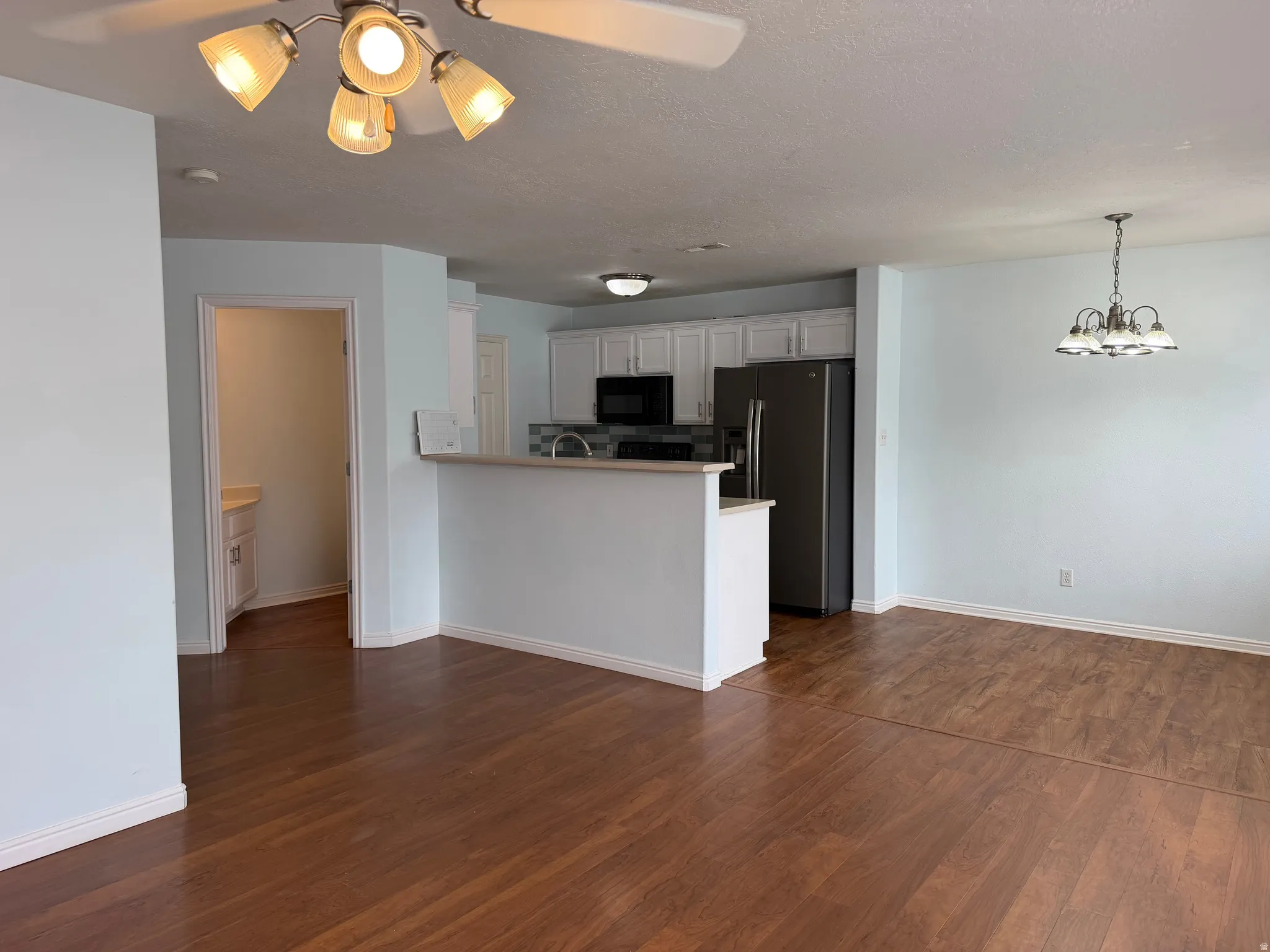 Wood-finish flooring throughout, kitchen with white cabinetry and stainless steel appliances, breakfast bar, and a chandelier in the dining area
