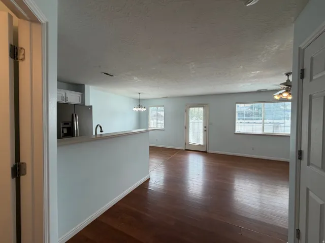Wood-finish flooring throughout, stainless steel refrigerator, white cabinetry, ceiling fan with integrated lighting, and multiple windows
