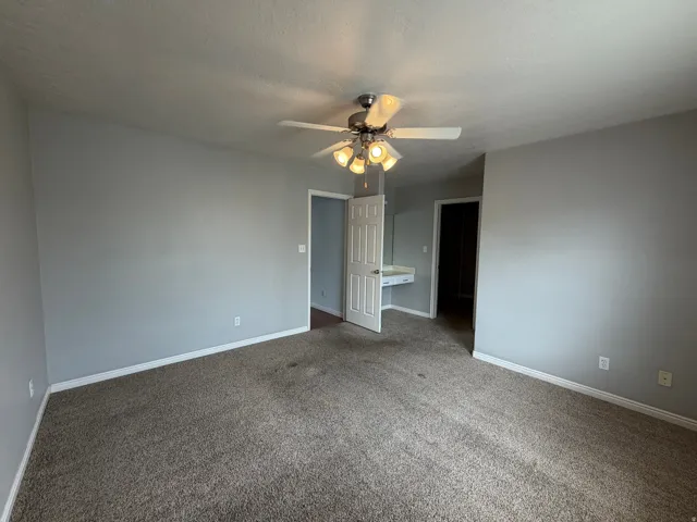 Neutral-toned walls, carpet flooring, a ceiling fan with integrated lighting, and a built-in vanity